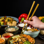 close-up-person-s-hand-taking-thai-food-with-chopsticks-against-black-background